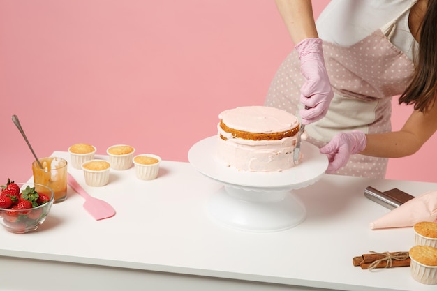 Nahaufnahme, kurz geschnittener Koch, Konditor oder Bäcker in weißem T-Shirt, der am Tisch kocht, isoliert auf rosa Pastellhintergrund im Studio. Kuchenherstellungsverfahren zum Auftragen von Sahne. Mock-up Copy Space Food-Konzept.