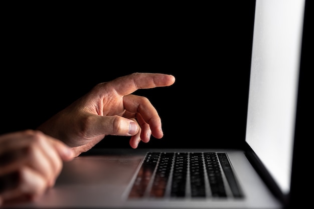 Nahaufnahme, männliche Finger zeigen auf Laptop-Bildschirm im Dunkeln.