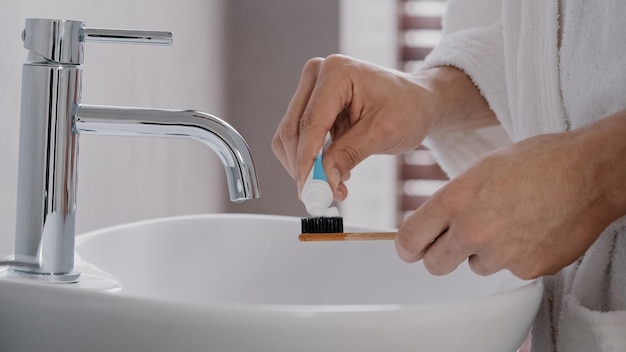 Nahaufnahme männlicher Hände im Bademantel mit Bambus-Holz-Zahnzähler, der das Bleaching-Röhrchen herausdrückt