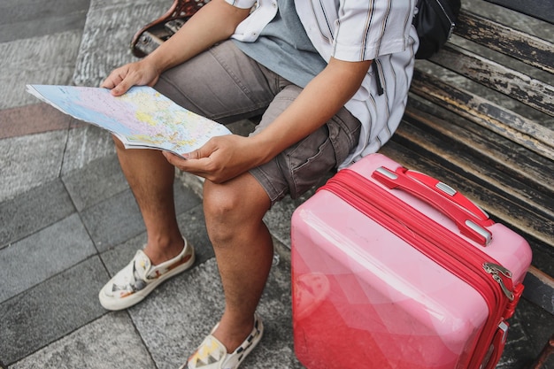 Nahaufnahme männlicher Reisenderhände, die mit Koffer auf dem Stuhl sitzen und Karte halten.