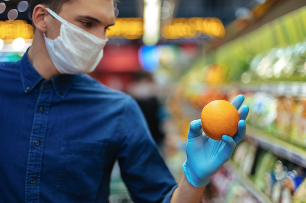 Nahaufnahme. Mann in einer Schutzmaske bei der Auswahl von Orangen im Supermarkt. Hygiene und Gesundheitsvorsorge