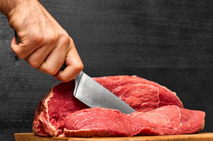 Nahaufnahme Mannhand, die ein Rindfleischfleisch mit einem Messer auf einem schwarzen Hintergrund schneidet