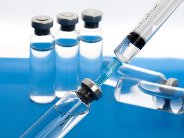 Nahaufnahme medizinische Spritze und Fläschchen mit Medikamenten zur Injektion auf weißem blauem Hintergrund