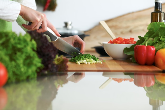 Nahaufnahme menschlicher Hände, die Gemüsesalat in der Küche auf dem Glastisch mit Reflexion kochen. Gesundes Essen und vegetarisches Konzept