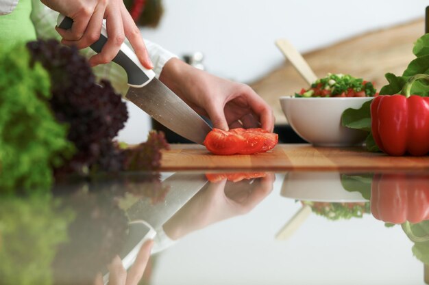 Nahaufnahme menschlicher Hände, die Gemüsesalat in der Küche auf dem Glastisch mit Reflexion kochen. Gesundes Essen und vegetarisches Konzept