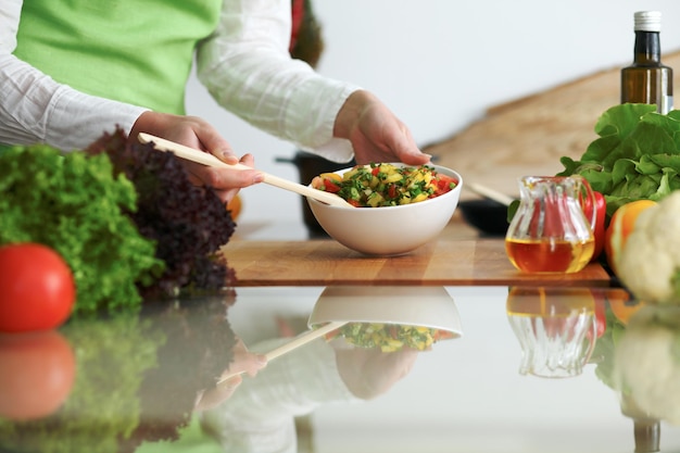 Nahaufnahme menschlicher Hände, die Gemüsesalat in der Küche auf dem Glastisch mit Reflexion kochen. Gesundes Essen und vegetarisches Konzept