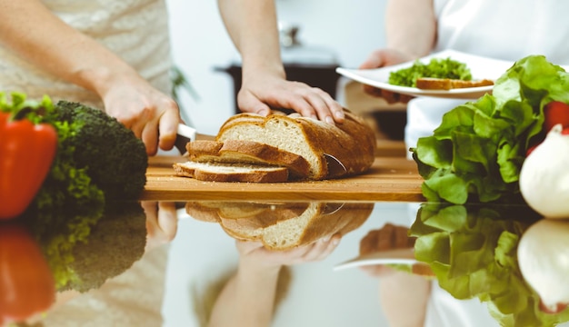 Nahaufnahme menschlicher Hände, die in der Küche kochen. Mutter und Tochter oder zwei Freundinnen schneiden Brot zum Abendessen. Freundschaft, Familie und Lifestyle-Konzepte.