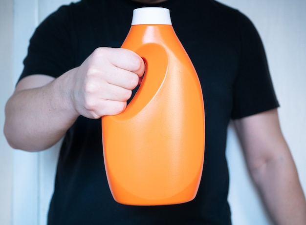 Nahaufnahme orangefarbene Plastikflasche Waschmittel oder Waschmaschinengel in der Hand des Mannes.