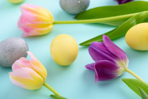 Nahaufnahme Osterkomposition von lila und rosa Tulpen und Ostereiern auf blauem Hintergrund