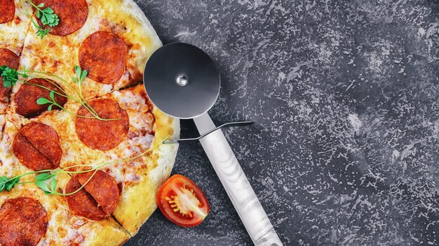 Nahaufnahme peperonipizza mit tomaten und rollenmesser auf betonoberfläche, draufsicht, kopierraum