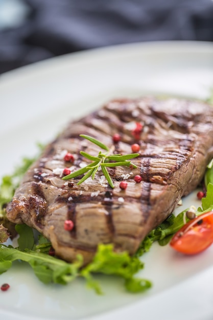 Nahaufnahme Portion saftiges Flankensteak aus Gemüsesalat Salzpfeffer und Rosmarin auf weißem Teller.