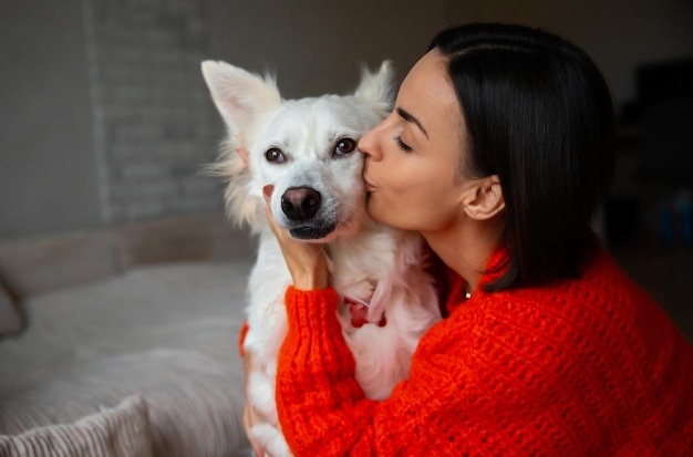 Nahaufnahme Porträt einer glücklichen schönen jungen Frau umarmt ihren großen weißen süßen Hund, während sie auf dem Teppich zu Hause liegt