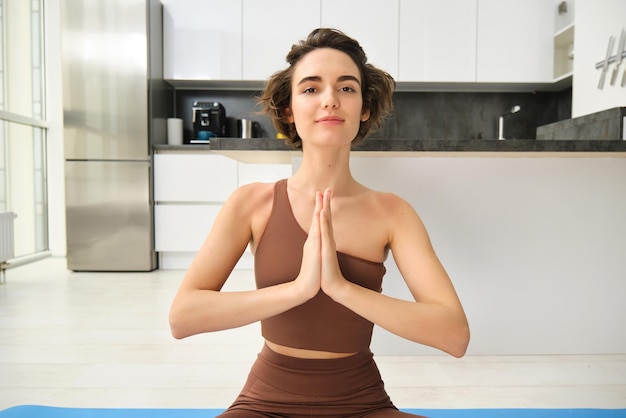 Nahaufnahme Porträt einer jungen Frau, die zu Hause sitzt und meditiert und Yoga praktiziert, indem sie Lotus-Pose macht