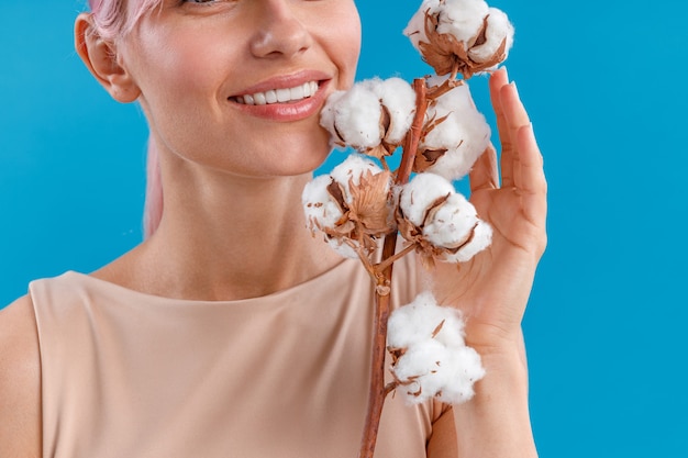 Nahaufnahme Porträt einer lächelnden Frau, die Zweig mit flauschigen Baumwollblumen in der Nähe ihres Gesichts hält