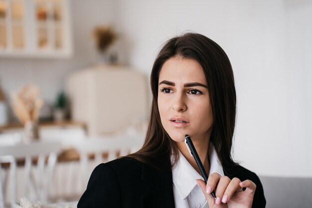 Foto nahaufnahme porträt einer nachdenklichen jungen brünetten geschäftsfrau, die wegschaut und ihr kinn mit dem stift berührt