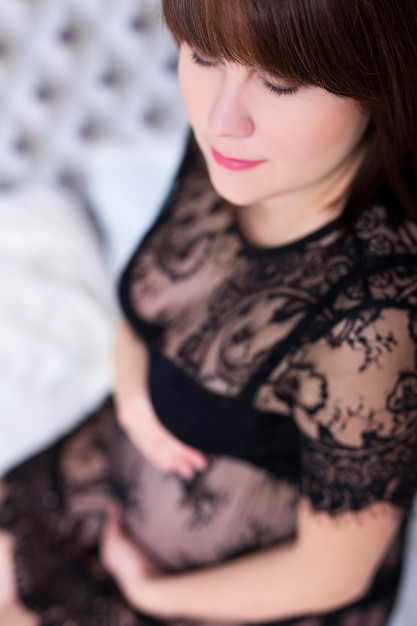 Nahaufnahme Porträt einer schönen schwangeren Frau, die auf dem Bett sitzt