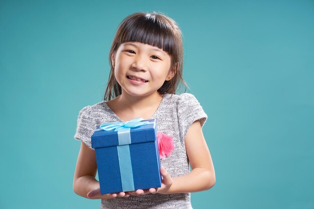 Nahaufnahme Porträt eines asiatischen kleinen glücklichen Mädchens mit blauer Geschenkbox isoliert auf hellblauem Hintergrund