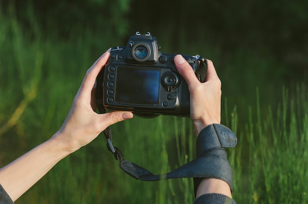 Nahaufnahme, professionelle Foto-Video-Kamera in den Händen eines Mädchens. Vor dem Hintergrund grüner Natur und Wald.