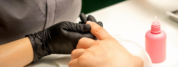 Nahaufnahme professioneller Maniküremeister hält die weibliche Hand des Kunden und desinfiziert Nägel in einem Nagelstudio