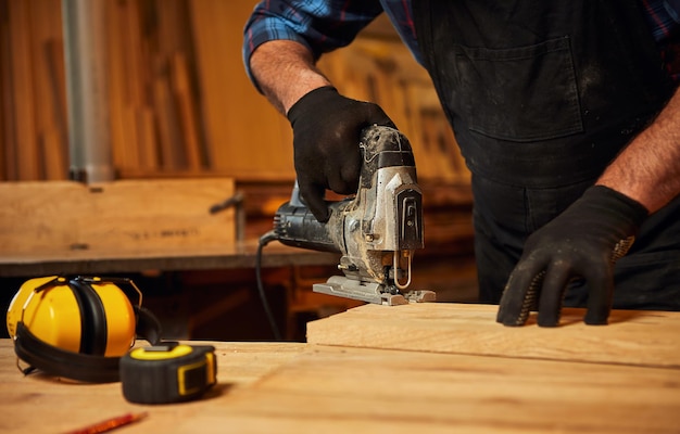 Nahaufnahme professioneller Tischlerhände, die Holz mit einer elektrischen Stichsäge in der Tischlerei sägen