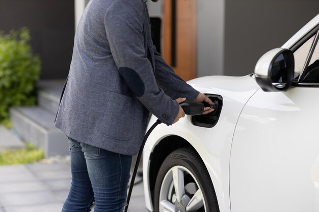 Nahaufnahme progressiver asiatischer mann lädt sein EV-auto an der ladestation zu hause auf