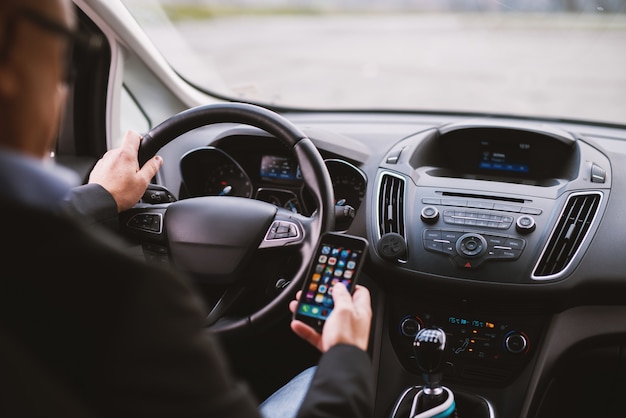 Nahaufnahme reifen eleganten professionellen eleganten Geschäftsmann in einem Anzug fährt ein Auto und SMS am Telefon.