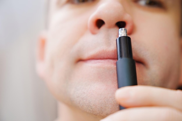 Nahaufnahme schneidet ein Mann seine Nasenhaare mit einem Trimmer