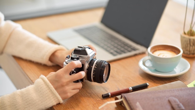 Nahaufnahme, schöne tausendjährige Fotografin auf dem Schreibtisch mit ihrer Vintage-Retro-Kamera.