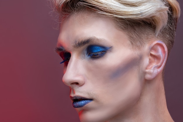 Nahaufnahme-Schönheitsporträt eines jungen Mannes mit professionellem Make-up, blondem Haar