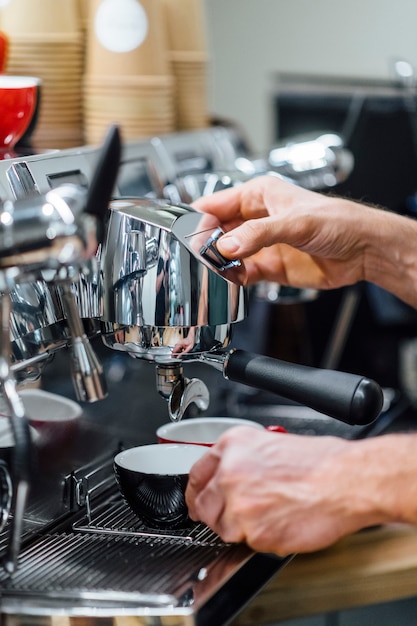 Nahaufnahme Schuss von Barista, der Filterhalter hält, während Kaffeemaschine frischen Espresso in Glas braut