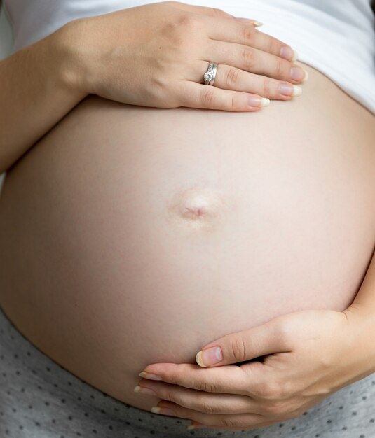 Nahaufnahme schwangere Frau Händchen haltend auf dicken Bauch