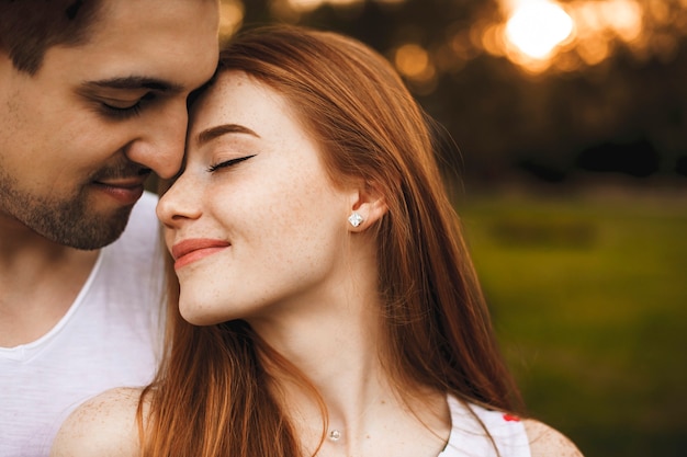 Nahaufnahme Seitenansicht Porträt eines erstaunlichen Paares, das eng mit geschlossenen Augen umarmt, die gegen Sonnenuntergang draußen während der Datierung lächeln.