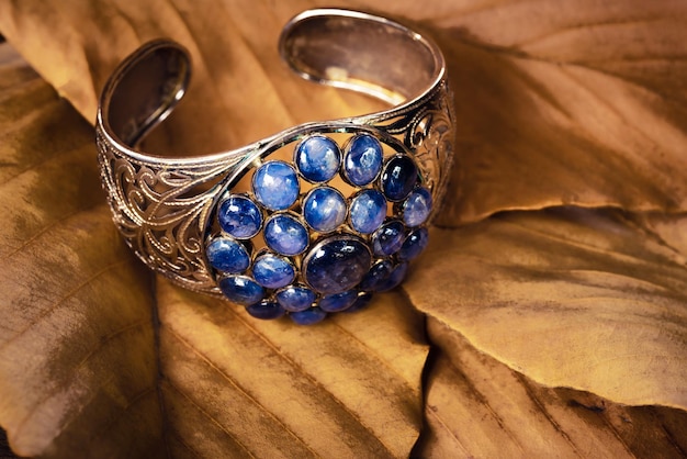 Nahaufnahme silberner Armreif mit blauem Edelsteinschmuck auf Blatthintergrund. Vintage-Armreif, alter Schmuck, verwendet für Vintage-Hintergrund