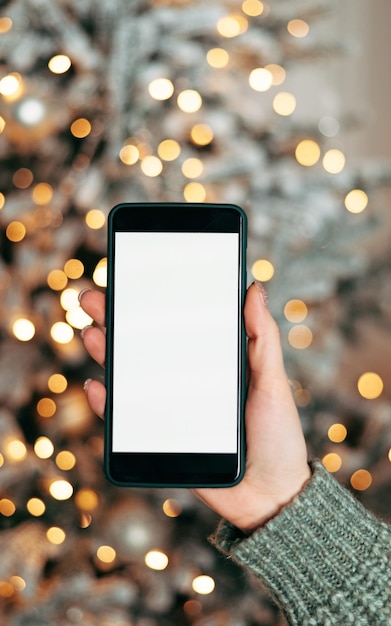 Nahaufnahme-Smartphone mit leerem Bildschirmmodell auf Feiertagshintergrund mit Weihnachtsbaumkunden