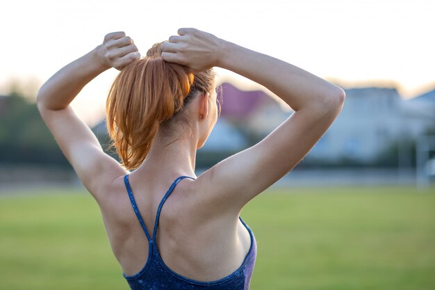 Nahaufnahme sportiver Frau Yongs mit dem roten Haar, das draußen mit den angehobenen Armen genießen Sonnenaufgang vor der Ausbildung steht.