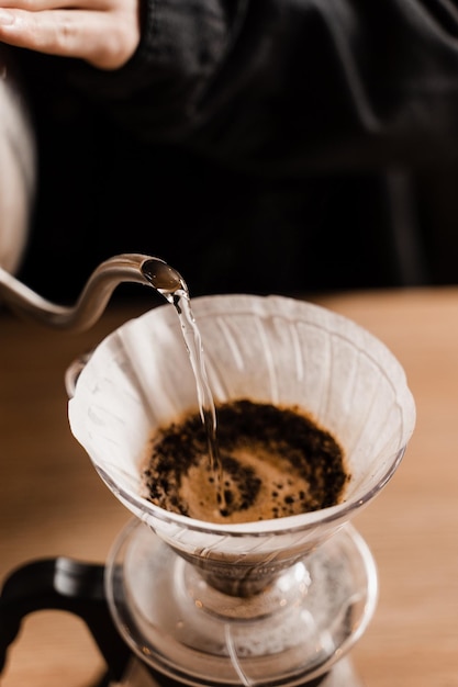 Nahaufnahme über Filter mit gemahlenem Kaffee im Trichter im Fokus Brühen von Filterkaffee tropfen Über eine alternative Methode zum Gießen von Wasser über geröstete und gemahlene Kaffeebohnen im Filter gießen