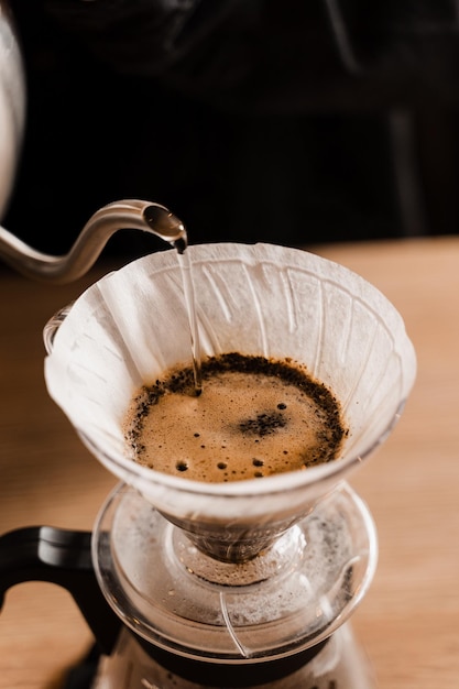 Nahaufnahme über Filter mit gemahlenem Kaffee im Trichter im Fokus Brühen von Filterkaffee tropfen Über eine alternative Methode zum Gießen von Wasser über geröstete und gemahlene Kaffeebohnen im Filter gießen