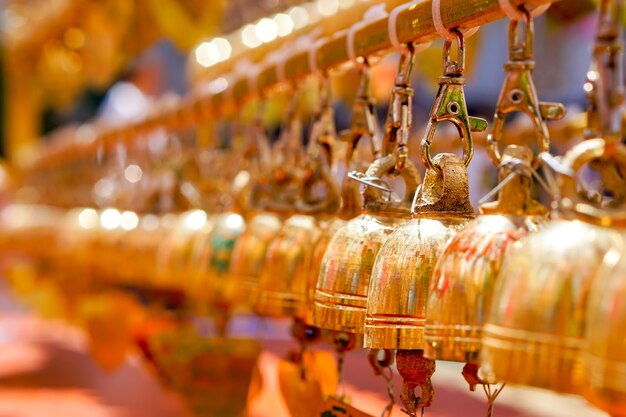 Nahaufnahme und perspektivische Ansicht Gruppe von kleinen goldenen Glocken hängen im thailändischen Tempel auf verschwommenem Hintergrund.