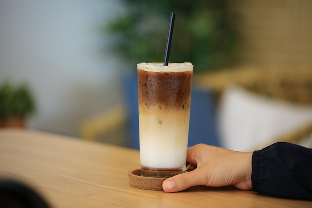 Nahaufnahme und selektive Fokushand, die ein Glas Eiskaramell-Macchiato auf einem Holztisch im Hochformat hält