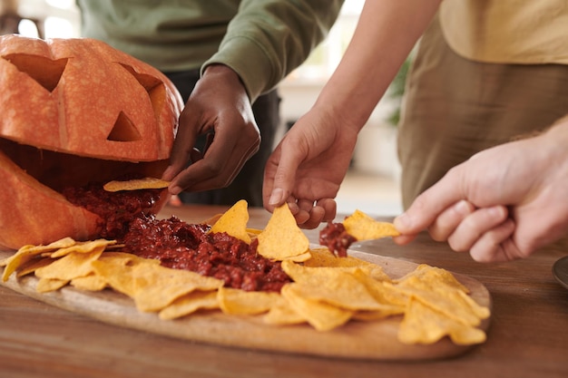 Nahaufnahme unkenntlicher interrassischer Freunde, die auf einer Halloween-Party Nachos mit Soße essen