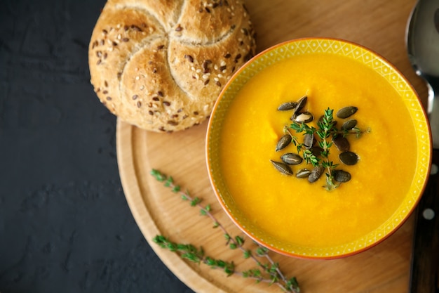 Nahaufnahme vegane hausgemachte Kürbissuppe mit Samen, Kräutern und Brötchen, auf einem schwarzen