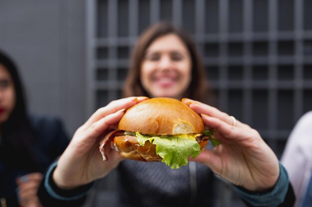 Nahaufnahme veganer Burger. Lächelnde verschwommene Frau auf dem Hintergrund, der Hamburger hält.