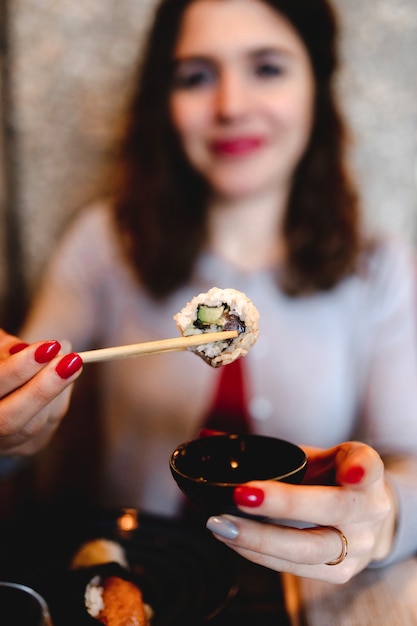 Nahaufnahme verschwommene Frau, die traditionellen japanischen Sushi-Rollenlachs mit Avocado hält, die zwischen Essstäbchen gelegt wird