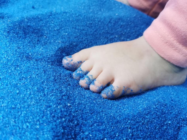 Nahaufnahme von Babyfüßen, die blauen Sand berühren