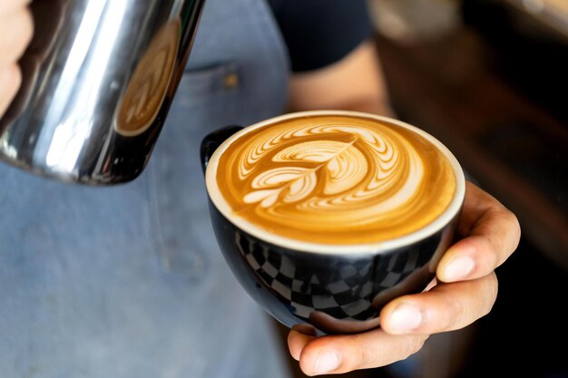 Nahaufnahme von Barista mit männlichen Händen, die Milch einschenken, um Kaffee Latte Art im Café zuzubereiten