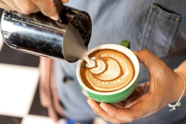 Nahaufnahme von Batistas männlichen Händen, die Milch einschenken, um Kaffee Latte Art im Café zuzubereiten