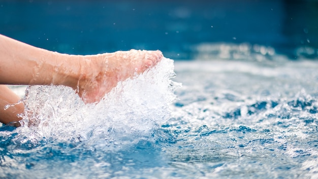 Nahaufnahme von Beinen und barfuß tretendem und spritzendem Wasser im Pool