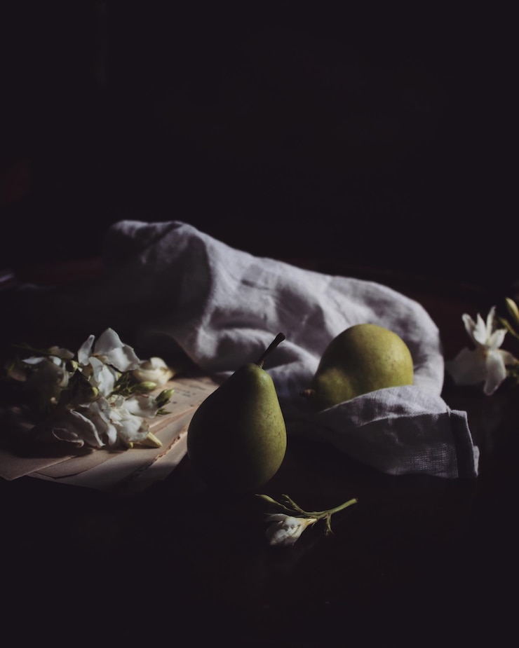 Foto nahaufnahme von birnen mit blumen und serviette auf tisch vor schwarzem hintergrund