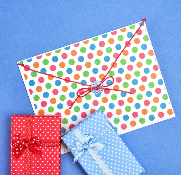 Nahaufnahme von blauen und roten Geschenkboxen mit Umschlag auf blauem Hintergrund Nette kleine Geschenke