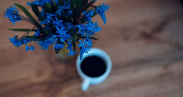 Nahaufnahme von blauen Veilchen auf Holztisch nahe Kaffeetasse.